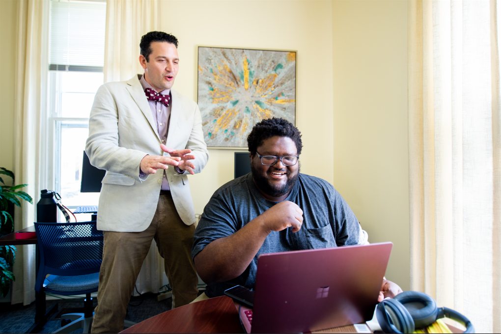 Consultant Looks at Laptop with Writer as Writer Smiles